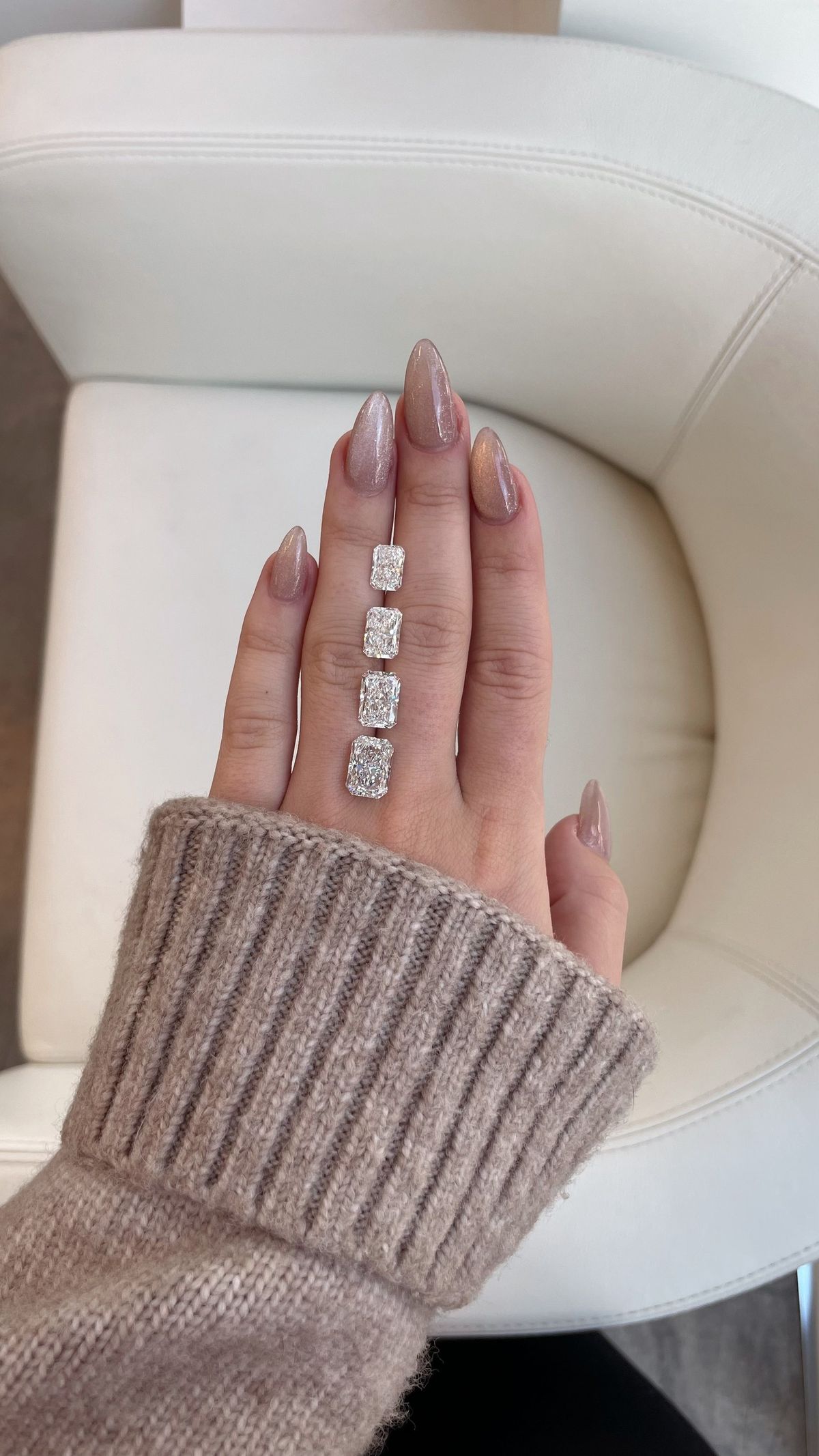 Four loose radiant cut diamonds lined up on a hand to compare sizes